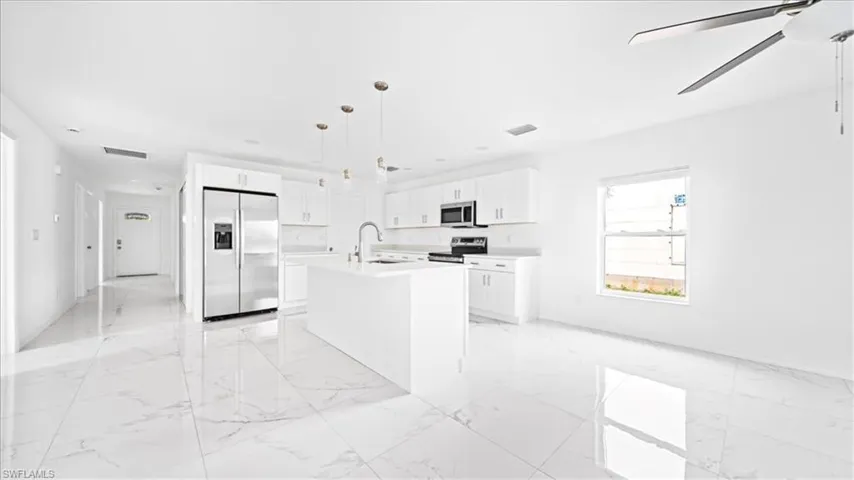 Kitchen with appliances with stainless steel finishes, light marble finish floors, white cabinetry, light countertops, and pendant lighting