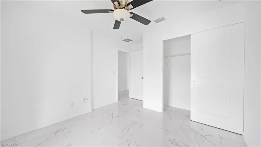 Unfurnished bedroom featuring ceiling fan, a closet, and light marble finish flooring
