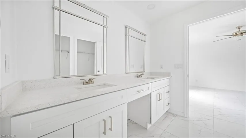 Full bathroom with light marble finish flooring, double vanity, a walk in closet, and ceiling fan