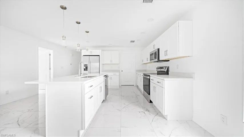 Kitchen featuring stainless steel appliances, white cabinets, hanging light fixtures, a kitchen island with sink, and light stone countertops
