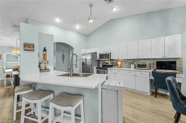 Kitchen with lofted ceiling, white cabinets, a kitchen bar, decorative light fixtures, and light wood finished floors