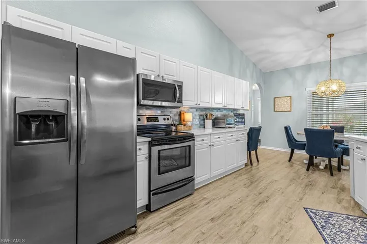 Kitchen with stainless steel appliances, arched walkways, white cabinets, hanging light fixtures, and a chandelier