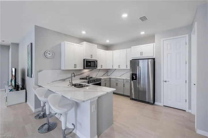 Kitchen with light stone counters, kitchen peninsula, backsplash, a kitchen bar, and appliances with stainless steel finishes