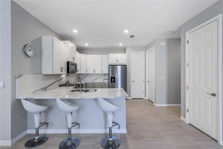 Kitchen with stainless steel appliances, light stone counters, white cabinetry, and kitchen peninsula