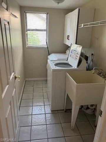 Laundry room featuring sink, light tile patterned flooring, separate washer and dryer, and cabinets