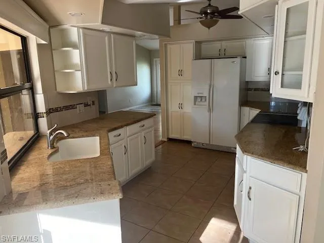 Kitchen with ceiling fan, backsplash, white refrigerator with ice dispenser, white cabinetry, and sink