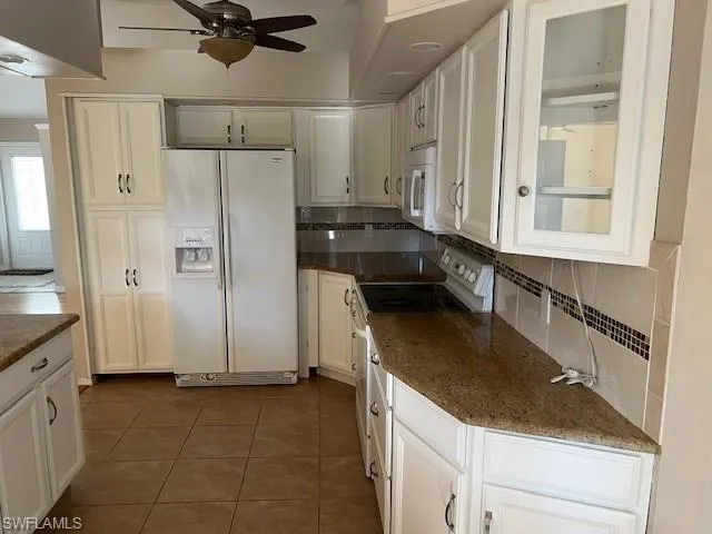 Kitchen with ceiling fan, tasteful backsplash, white cabinetry, dark tile patterned floors, and white appliances