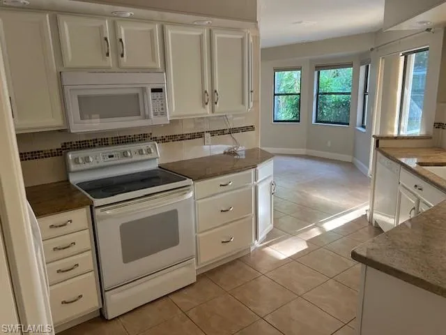 Kitchen featuring white cabinets, backsplash, white appliances, and light tile patterned floors