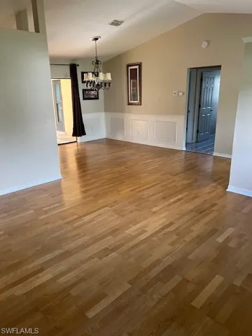 Spare room featuring lofted ceiling, hardwood / wood-style flooring, and a chandelier