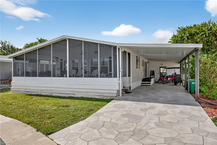 View of front of house featuring an attached carport, driveway, a front yard, and a sunroom