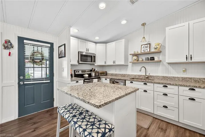 Kitchen with white cabinetry, open shelves, light stone countertops, a kitchen breakfast bar, and appliances with stainless steel finishes