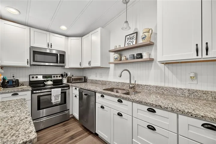 Kitchen with open shelves, appliances with stainless steel finishes, white cabinets, light stone countertops, and recessed lighting
