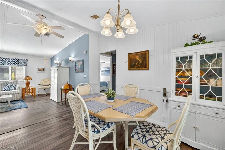 Dining space with a chandelier, vaulted ceiling, ceiling fan, dark wood-style flooring, and wooden walls