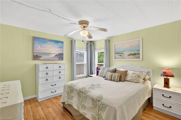 Bedroom with light wood-type flooring, wooden walls, and a ceiling fan