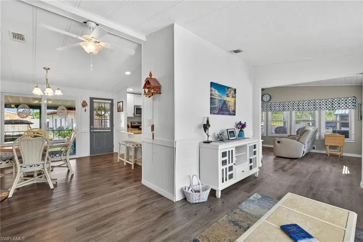 Living area featuring a ceiling fan, vaulted ceiling, dark wood-style flooring, a chandelier, and a decorative wall