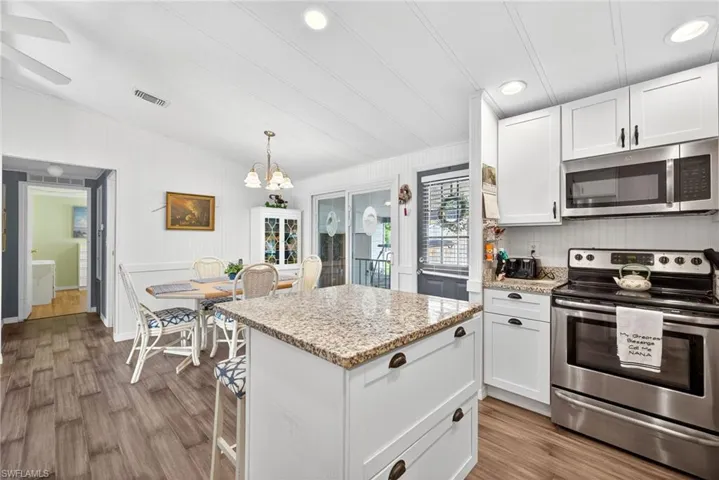Kitchen featuring stainless steel appliances, white cabinets, light stone countertops, dark wood-style flooring, and lofted ceiling