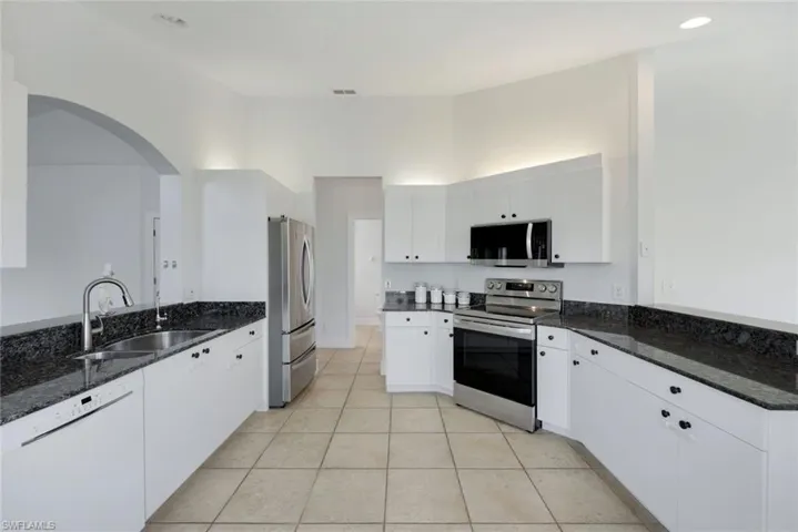 Kitchen with stainless steel appliances, sink, dark stone countertops, and white cabinets