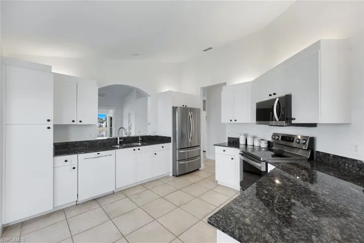 Kitchen featuring lofted ceiling, sink, white cabinetry, dark stone countertops, and stainless steel appliances