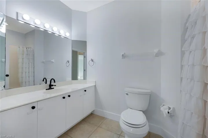 Bathroom featuring a shower with curtain, vanity, toilet, and tile patterned flooring