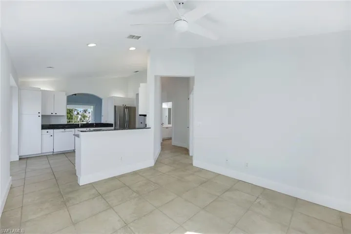 Kitchen with vaulted ceiling, stainless steel fridge, white cabinets, light tile patterned floors, and ceiling fan