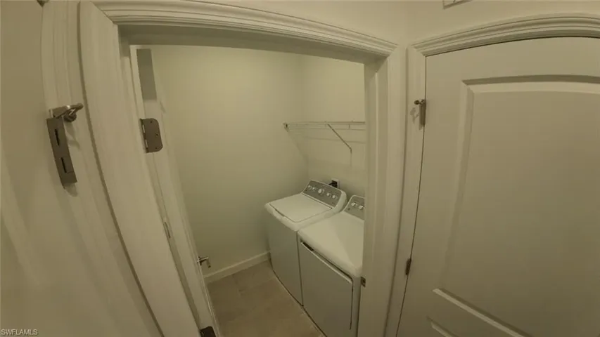 Laundry room with washer and clothes dryer and light tile patterned floors