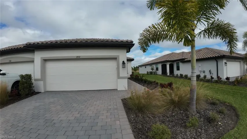 View of property exterior featuring decorative driveway, stucco siding, a lawn, a tiled roof, and an attached garage