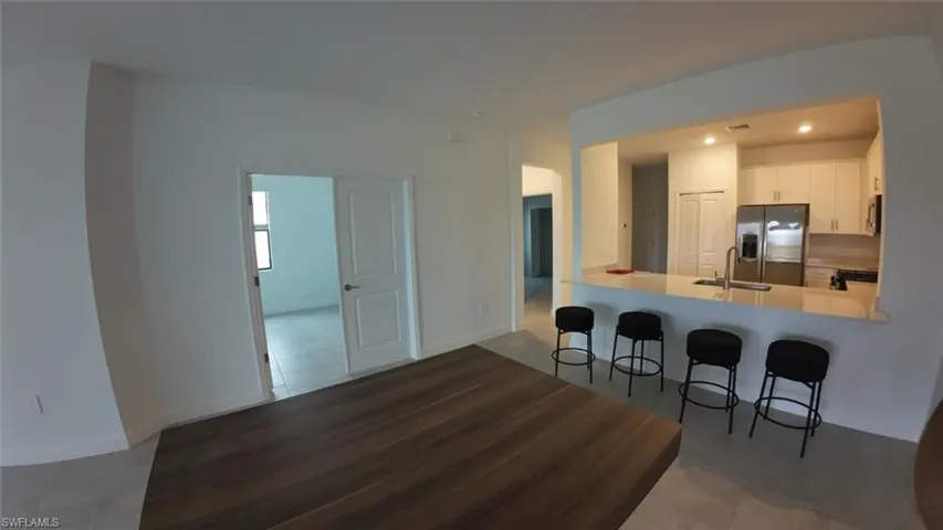 Kitchen featuring stainless steel fridge, a breakfast bar, a peninsula, white cabinetry, and recessed lighting