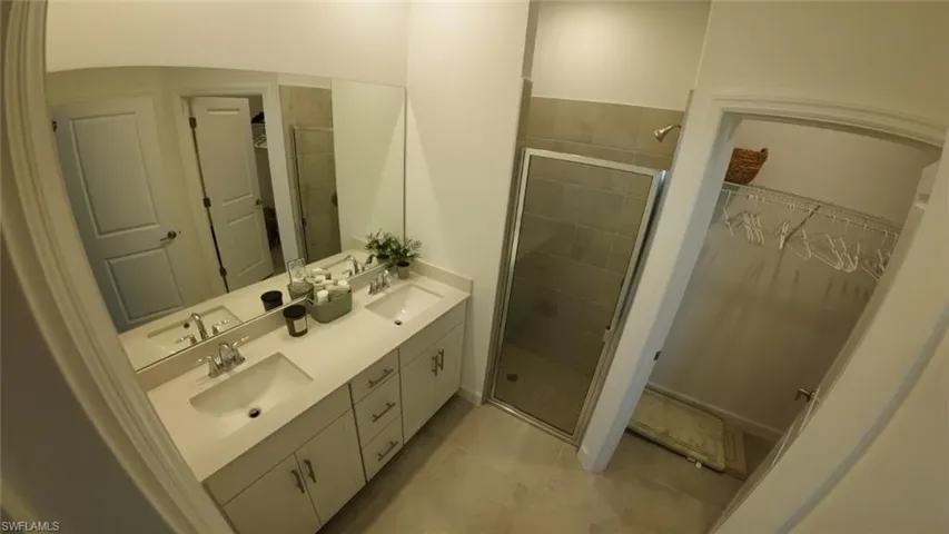 Full bathroom featuring a spacious closet, double vanity, a shower stall, and light tile patterned flooring
