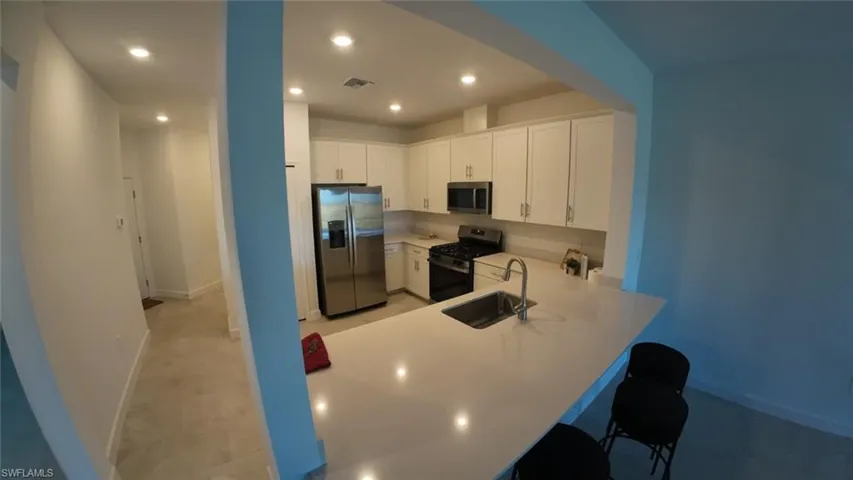 Kitchen featuring white cabinets, appliances with stainless steel finishes, a peninsula, a kitchen bar, and recessed lighting