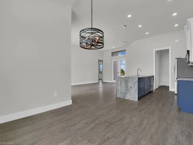 Kitchen with open floor plan, light stone counters, decorative light fixtures, dark wood-type flooring, and stainless steel appliances