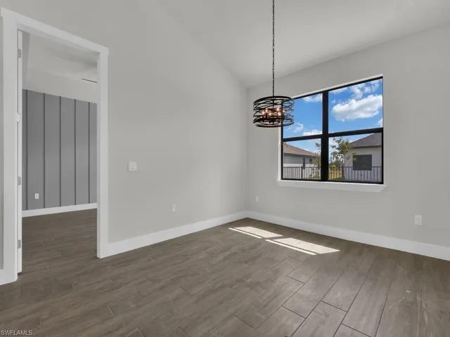 Spare room featuring vaulted ceiling, dark wood-style flooring, and a chandelier