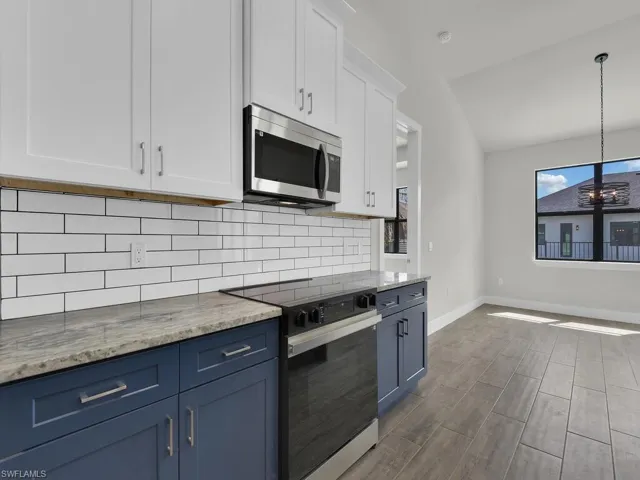 Two tone kitchen featuring black electric range oven, stainless steel microwave, light stone counters, decorative backsplash, and lofted ceiling