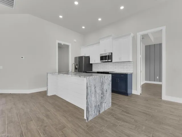 Two tone kitchen with light stone countertops, dark wood-type flooring, a center island with sink, two tone color scheme, and stainless steel appliances