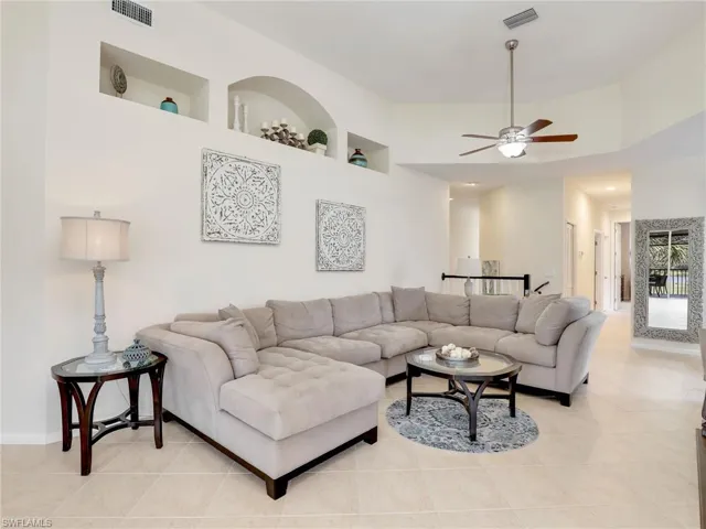 Living room featuring a towering ceiling, ceiling fan, built in features, and light tile patterned floors