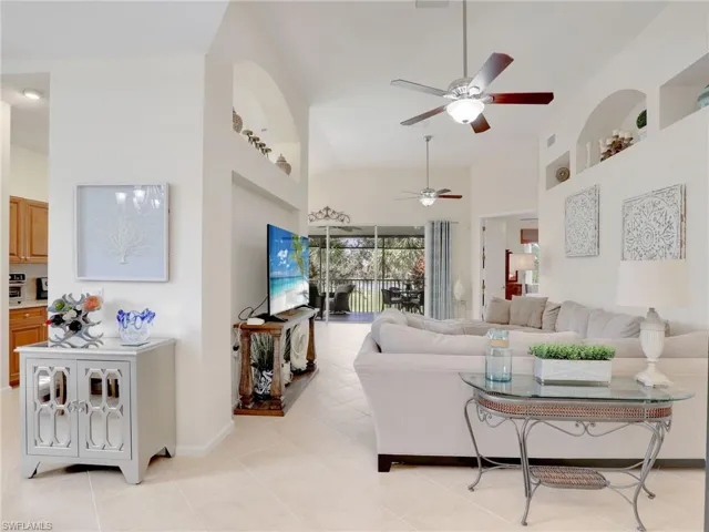 Living room with light tile patterned flooring, high vaulted ceiling, built in features, and ceiling fan