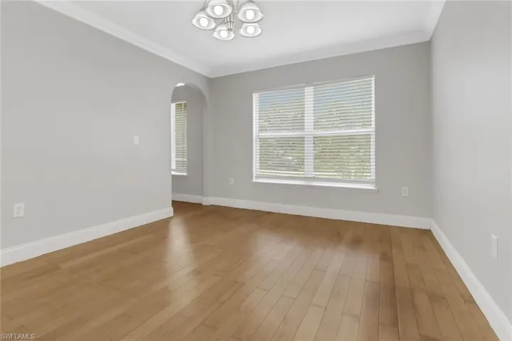 Empty room with a notable chandelier, crown molding, and light wood-type flooring
