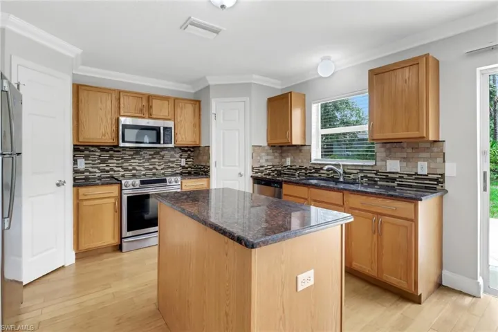 Kitchen with light hardwood / wood-style floors, tasteful backsplash, a kitchen island, and appliances with stainless steel finishes