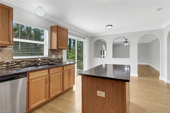 Kitchen with a kitchen island, dishwasher, backsplash, light wood-type flooring, and sink