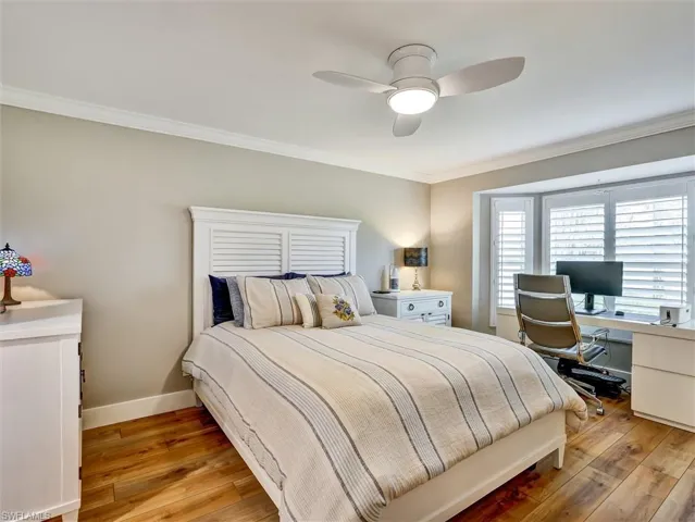 Bedroom with ornamental molding, light wood-type flooring, a ceiling fan, and a desk