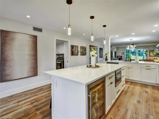 Kitchen featuring white cabinets, light wood-style flooring, hanging light fixtures, wine cooler, and a center island
