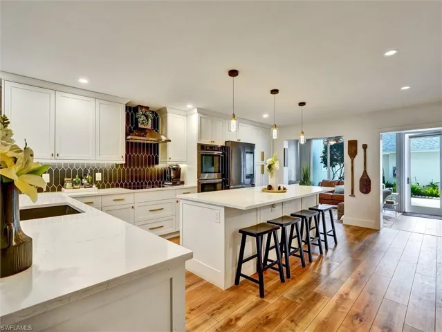 Kitchen featuring a center island, pendant lighting, light stone countertops, decorative backsplash, and a breakfast bar area