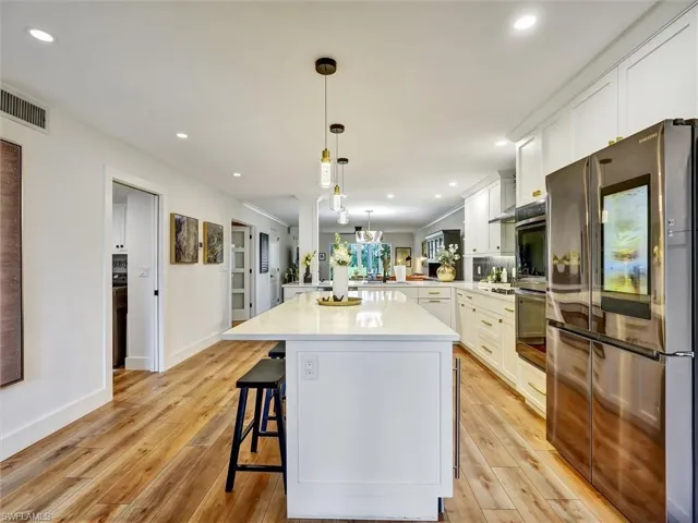 Kitchen featuring stainless steel appliances, white cabinetry, a breakfast bar, decorative light fixtures, and light wood-style flooring