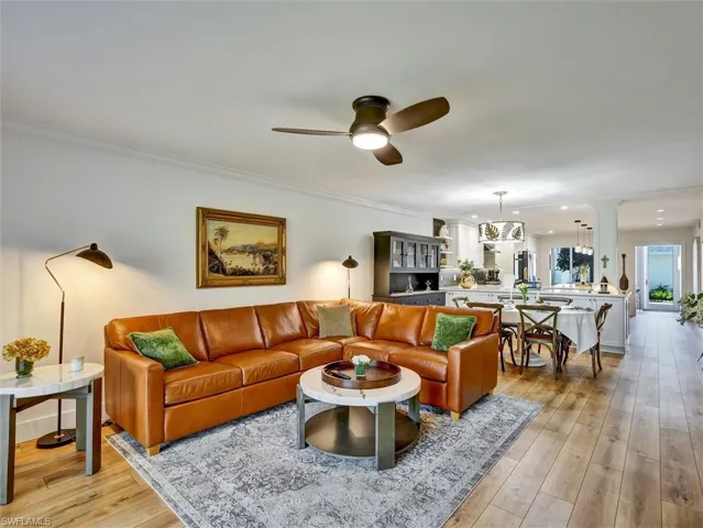 Living area with a ceiling fan, light wood finished floors, hanging lights, and crown molding