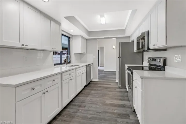 Kitchen featuring stainless steel appliances, white cabinets, sink, a raised ceiling, and wood-type flooring