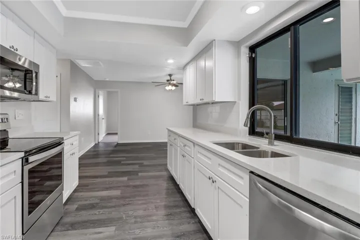 Kitchen with white cabinetry, ceiling fan, sink, appliances with stainless steel finishes, and dark wood-type flooring