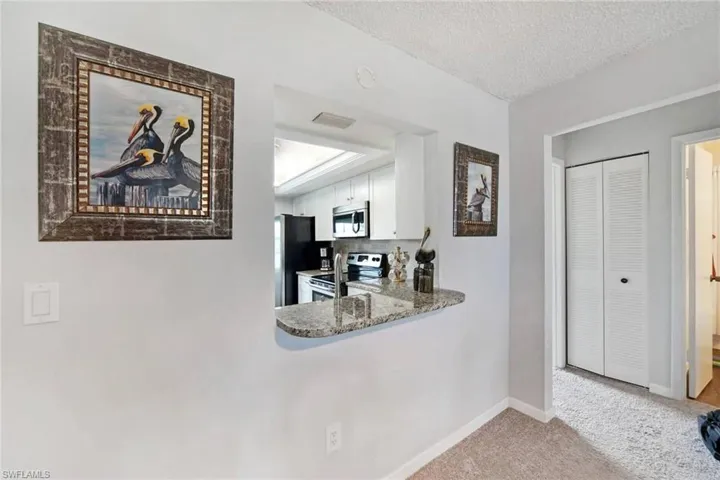 Kitchen featuring a textured ceiling, appliances with stainless steel finishes, white cabinetry, light carpet, and backsplash