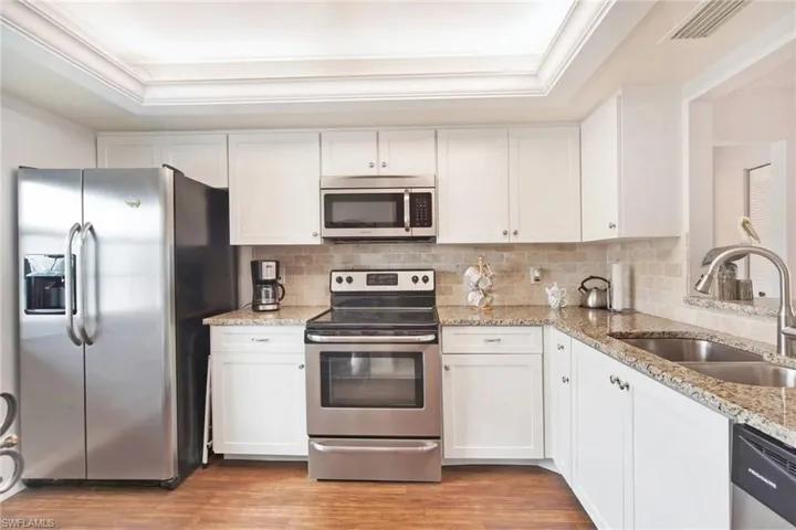 Kitchen featuring tasteful backsplash, a raised ceiling, sink, white cabinetry, and stainless steel appliances
