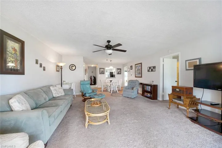 Carpeted living room featuring ceiling fan and a textured ceiling