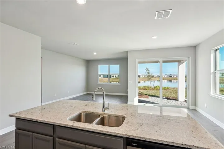 Kitchen featuring a water view, sink, stainless steel dishwasher, and light stone counters