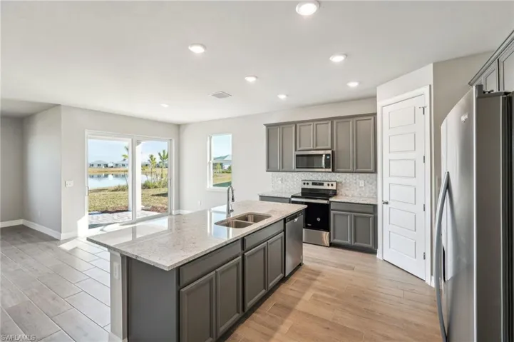 Kitchen featuring appliances with stainless steel finishes, an island with sink, sink, light stone counters, and a water view